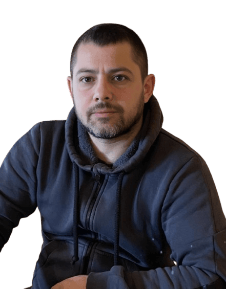 Man with a beard wearing a dark hoodie seated against a plain background.